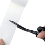 En Saks for kinesio- og sportstape som skjærer et stykke hvitt stoff for kinesio- og sportstape-applikasjoner.